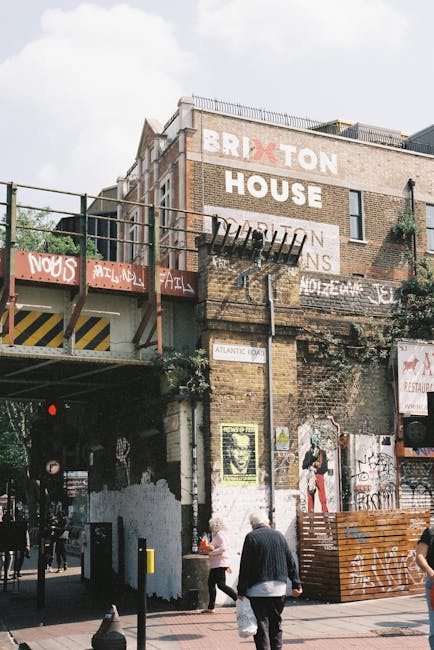 This image shows the exterior of a multi-story brick building in Brixton, with a prominent sign reading 'BRIXTON HOUSE' painted on the upper façade. The building features a fire escape ladder on the f